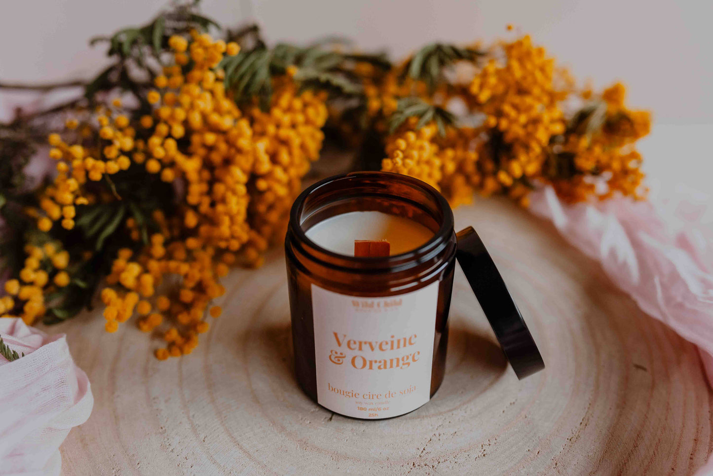 Vue rapprochée de la bougie “Verveine & Orange”, pot ambré avec mèche prête à l’allumage, décorée de fleurs séchées autour.