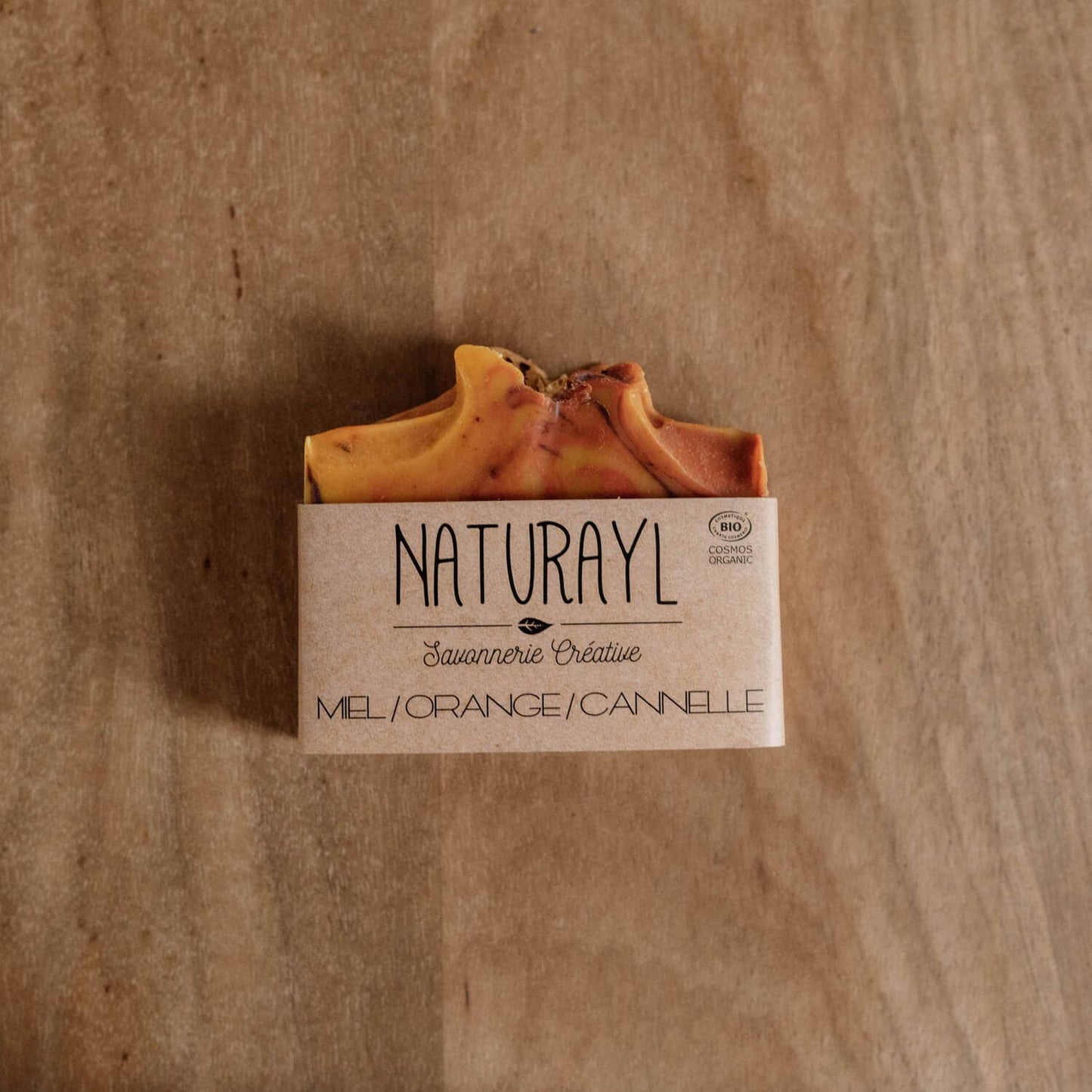 Savon artisanal Miel, Orange & Cannelle Naturayl présenté sur un fond en bois naturel, fabriqué à la main selon la méthode de saponification à froid.