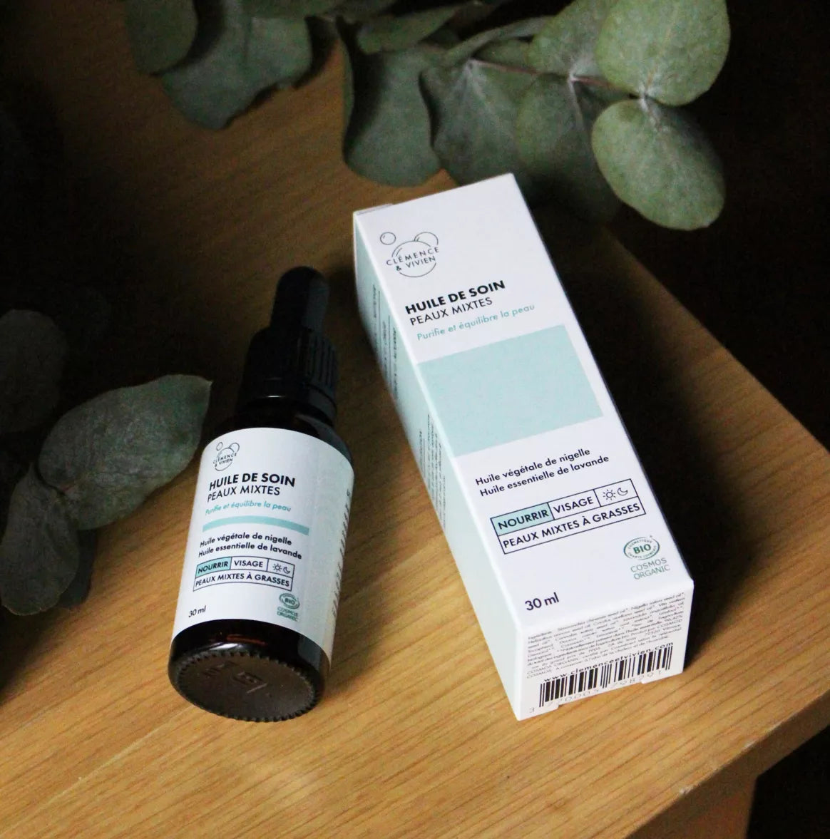 Huile de soin peaux mixtes Clémence & Vivien posée sur une table en bois, accompagnée de son étui, ambiance naturelle et végétale.
