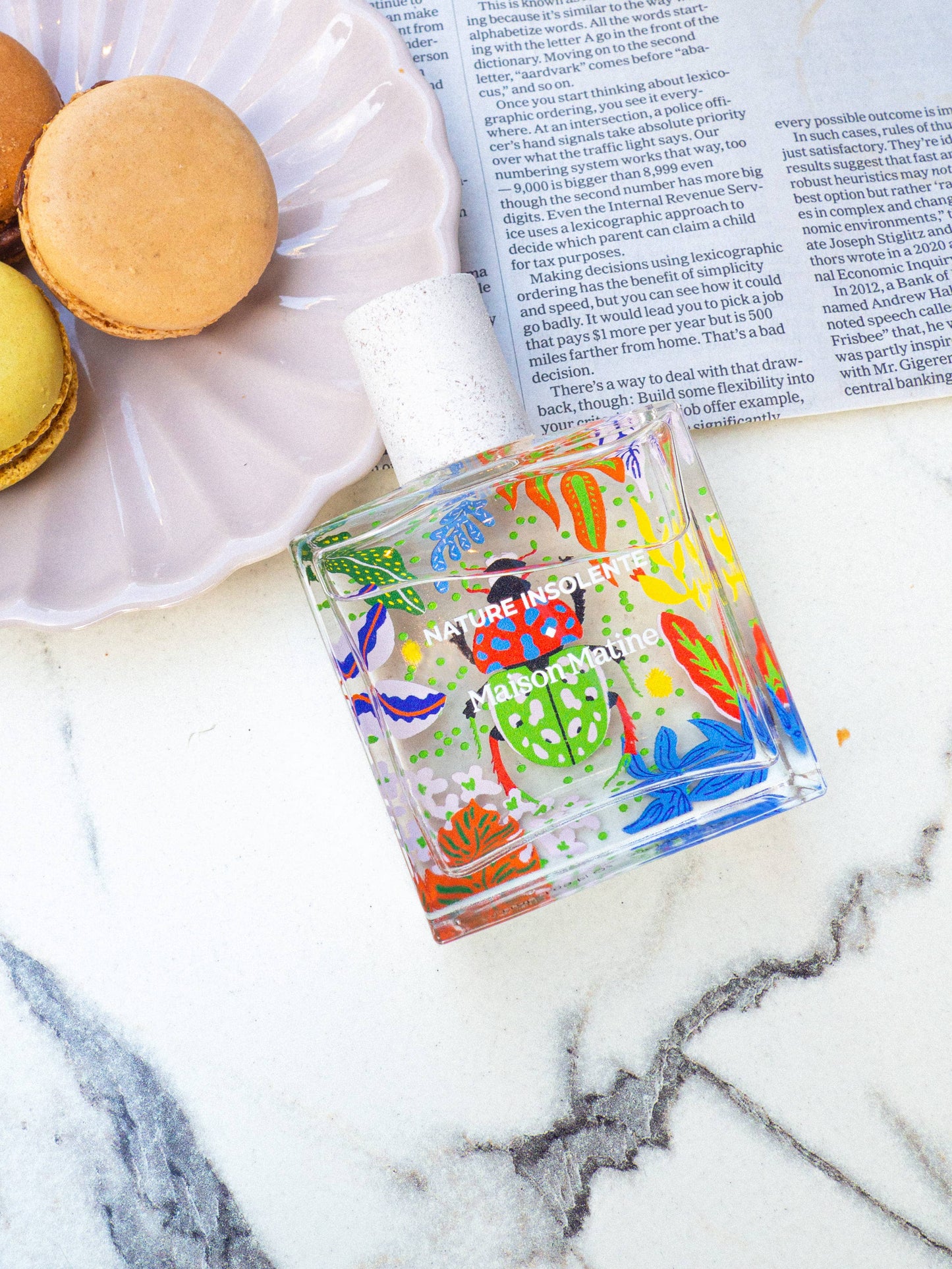 Flacon Nature Insolente posé sur une assiette de macarons, évoquant la douceur et la fraîcheur.