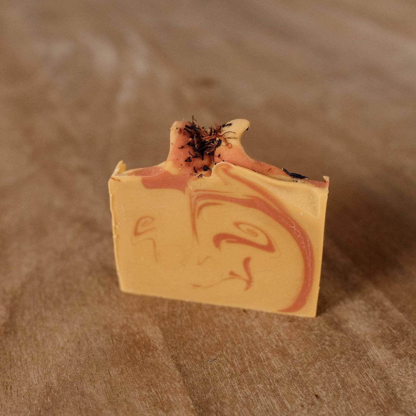 « Savon Naturayl Orient vue de côté, montrant les marbrures orientales orange et jaune et la fleur séchée décorative au sommet. »