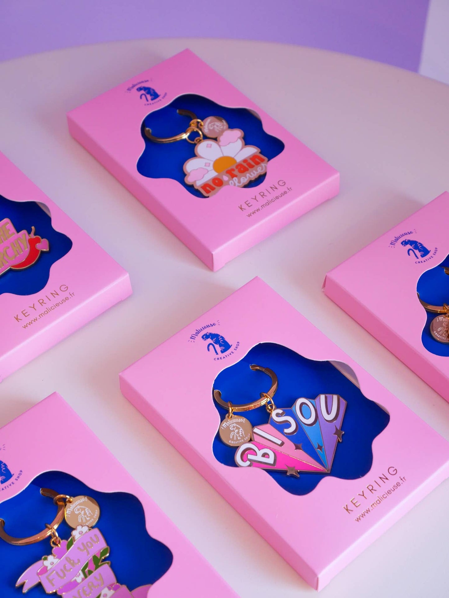 Gros plan des portes-clé dans le même esprit que « Burn the Patriarchy » rose et doré sur fond créatif.