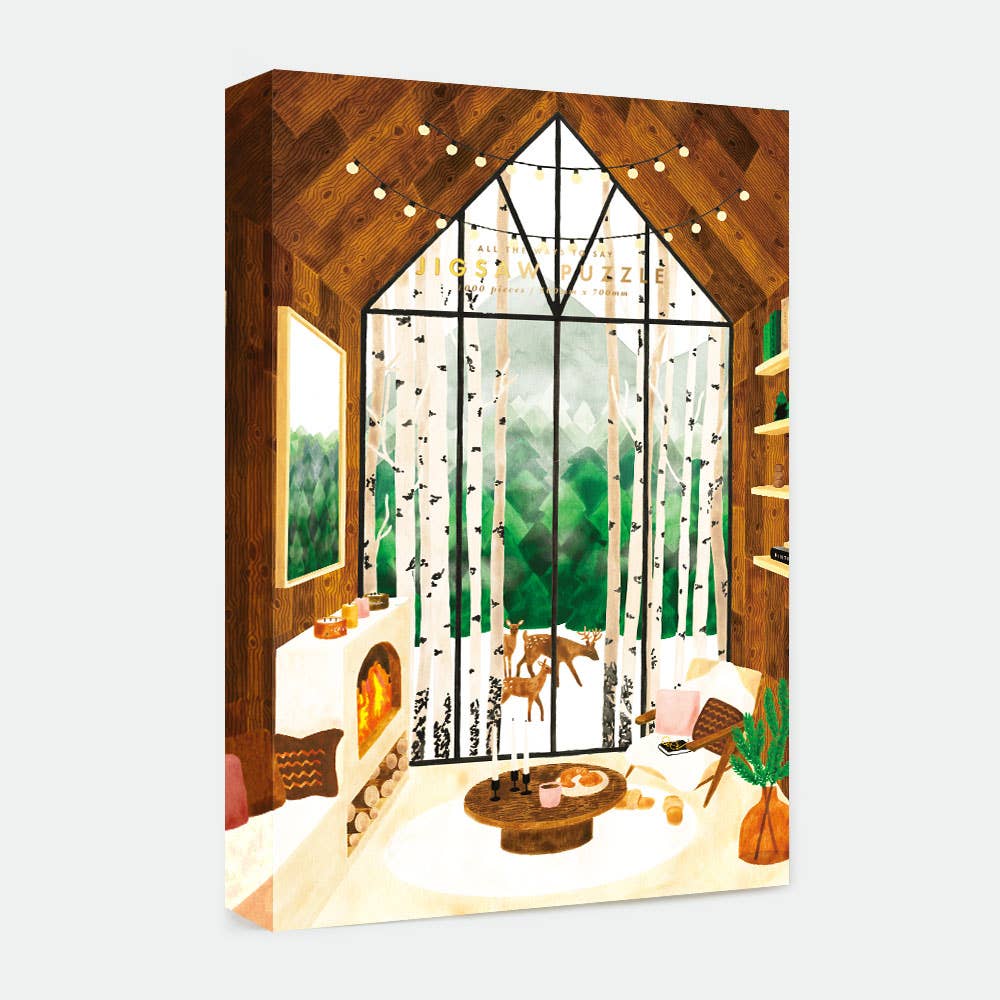 Boîte du puzzle Laponie 1000 pièces All The Ways To Say, illustrée d’un chalet en bois avec grandes baies vitrées donnant sur une forêt enneigée, ambiance chaleureuse et scandinave.