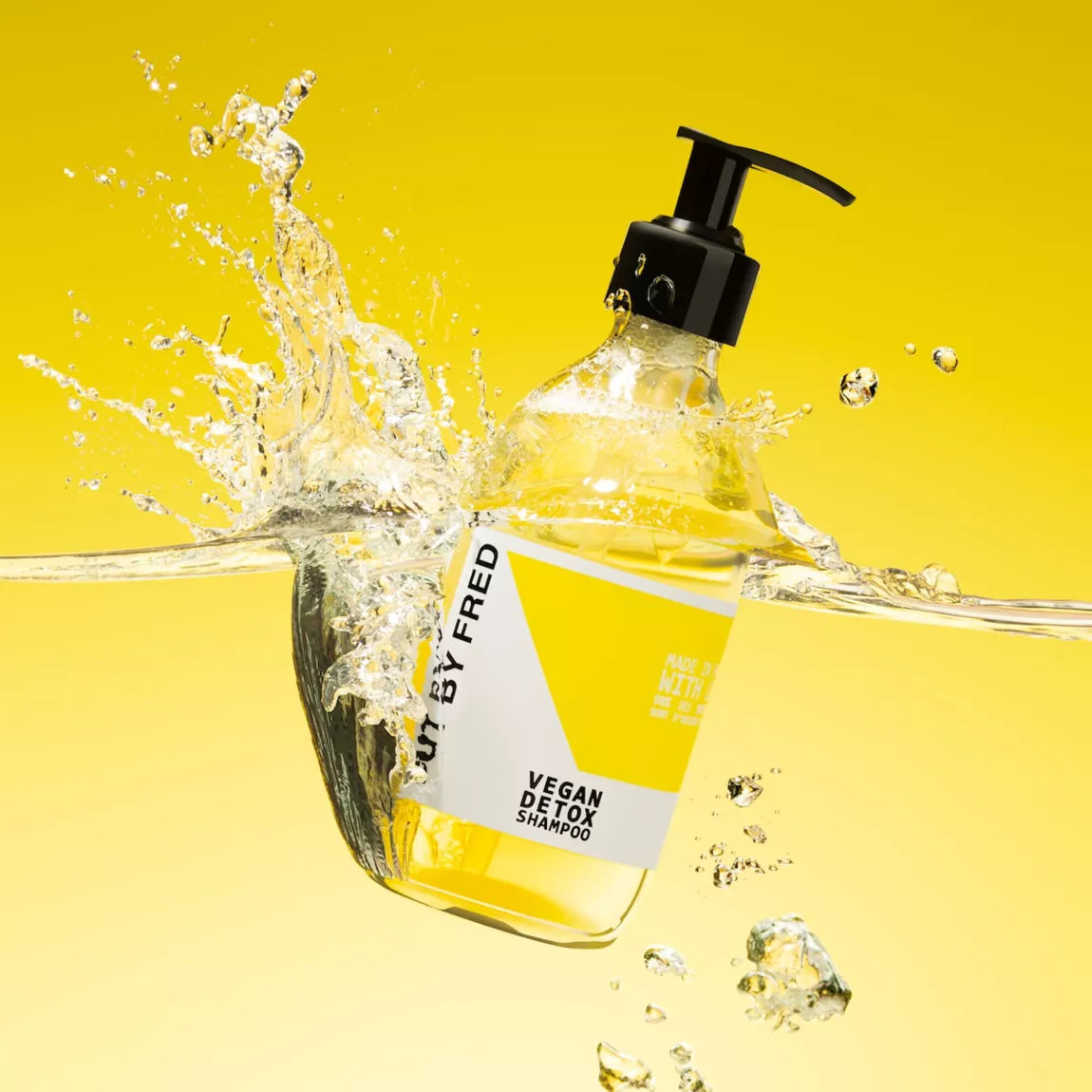 Vegan Detox Shampoo Cut By Fred, flacon transparent avec pompe noire plongé dans l’eau, effet éclaboussures dynamiques.