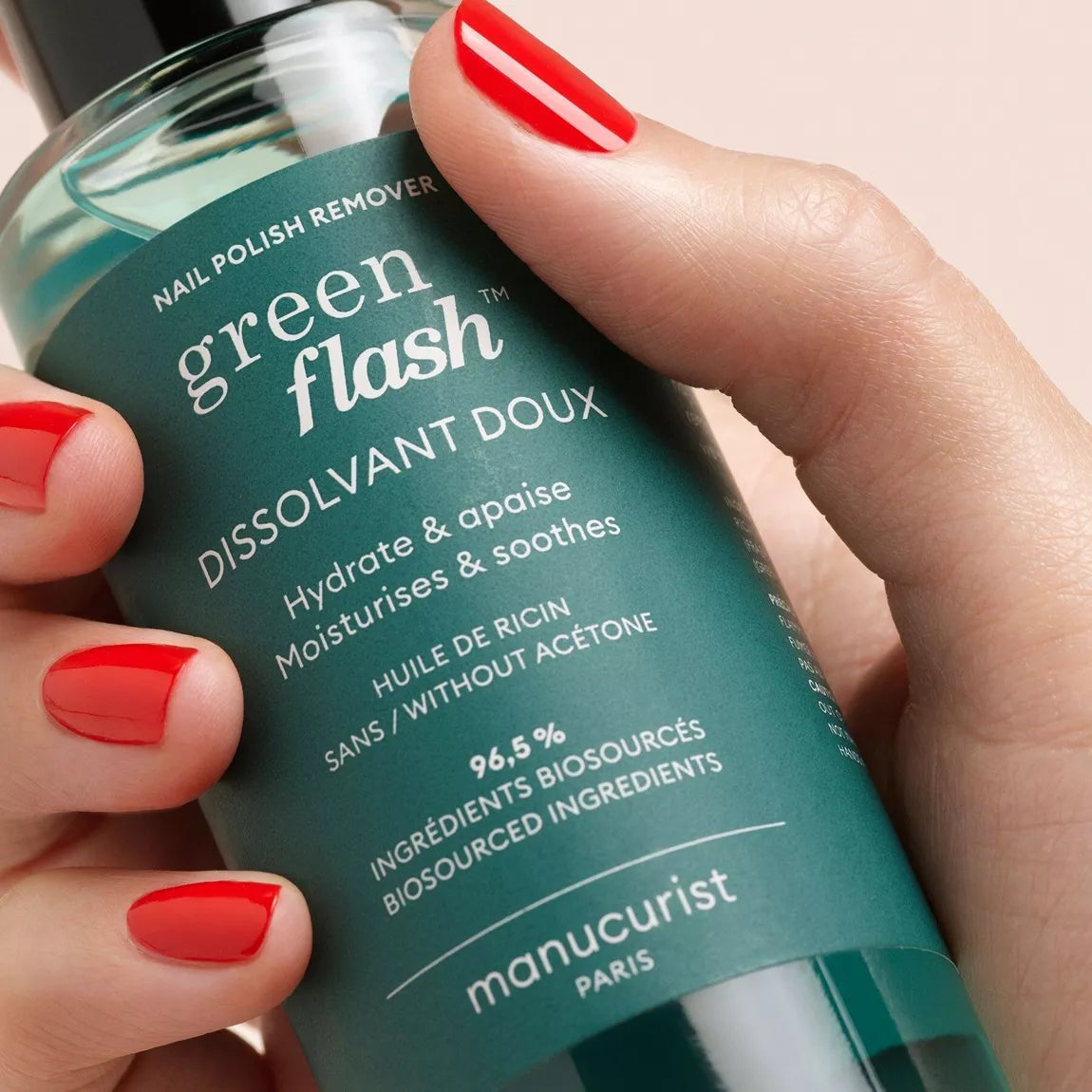Main aux ongles vernis rouge tenant le flacon de dissolvant doux Green Flash™ Manucurist, illustrant son utilisation facile et pratique.