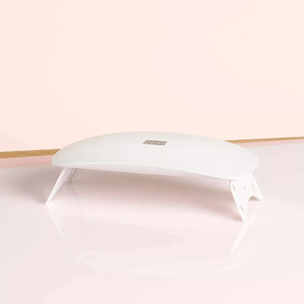 Lampe LED Slim Manucurist blanche, design ergonomique et pliable, posée sur une surface rose pâle.