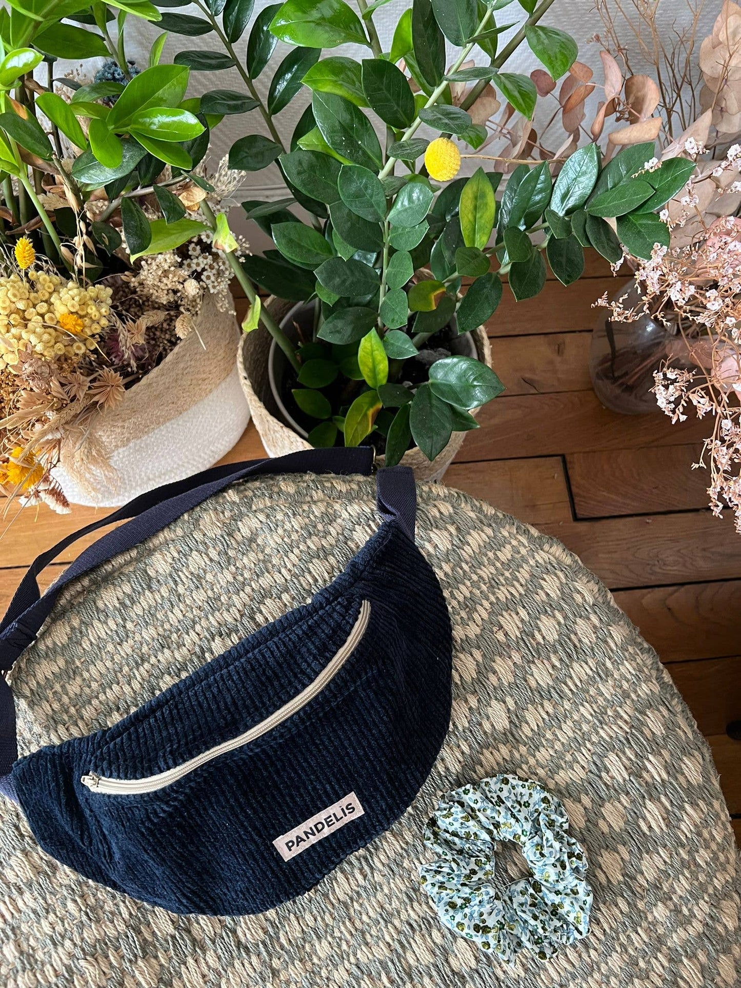 Banane Pandelis bleu marine en velours côtelé, posée sur une table ronde décorative avec une plante verte en arrière-plan.