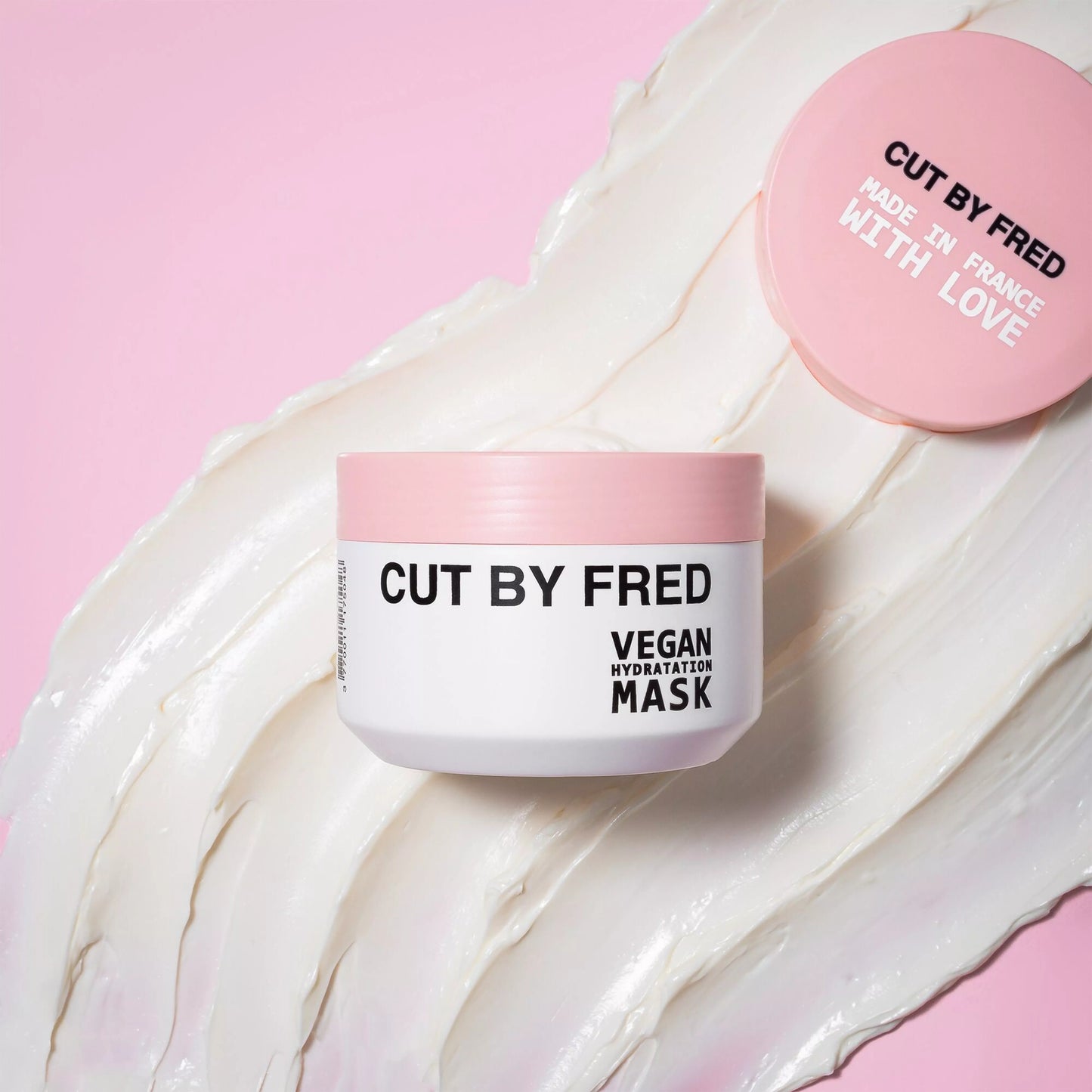 Pot du Vegan Hydratation Mask Cut By Fred avec texture crème capillaire étalée sur fond rose.