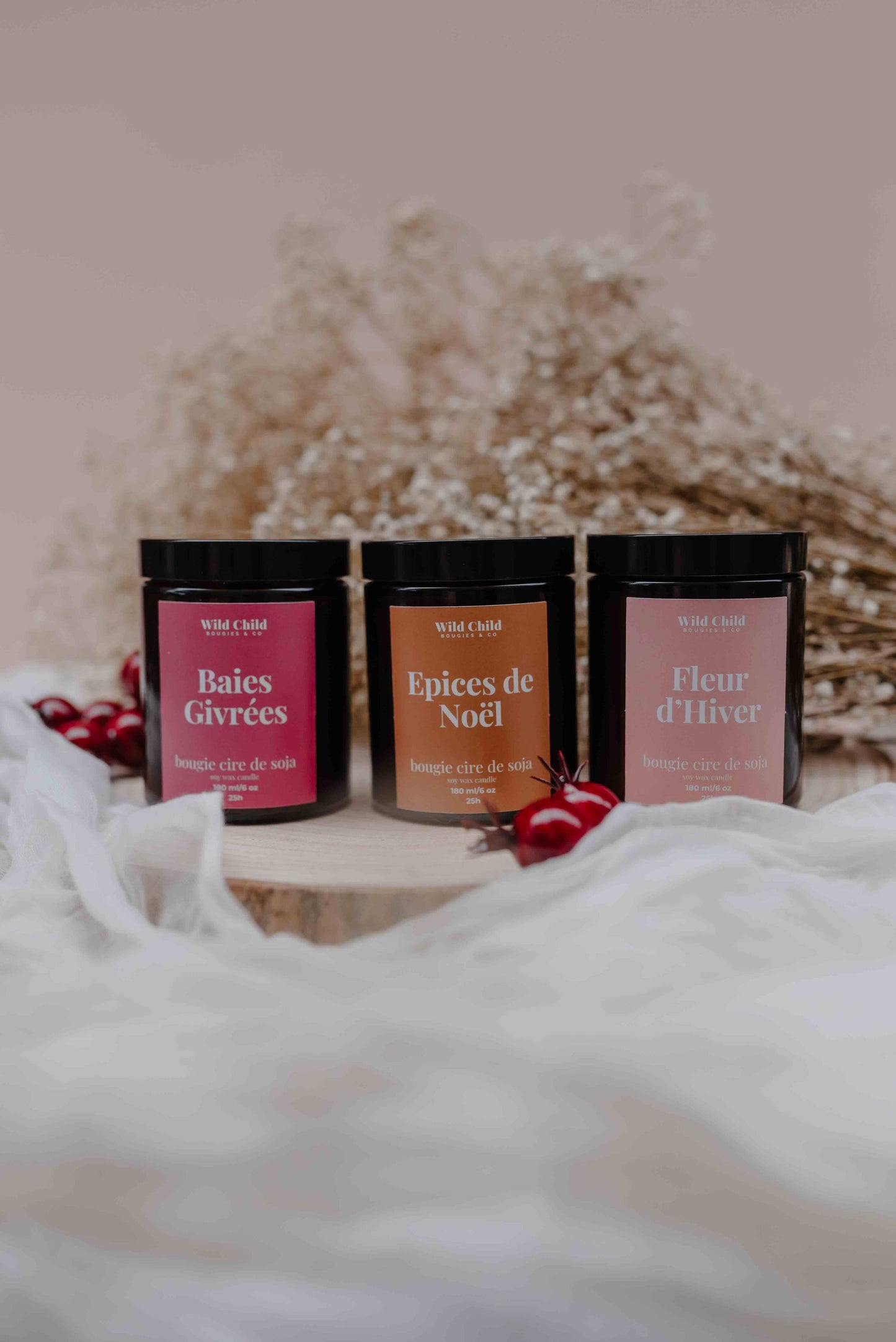 Trio de bougies parfumées Wild Child, dont Fleur d’Hiver, présentées sur fond hivernal avec gypsophile et baies rouges.
