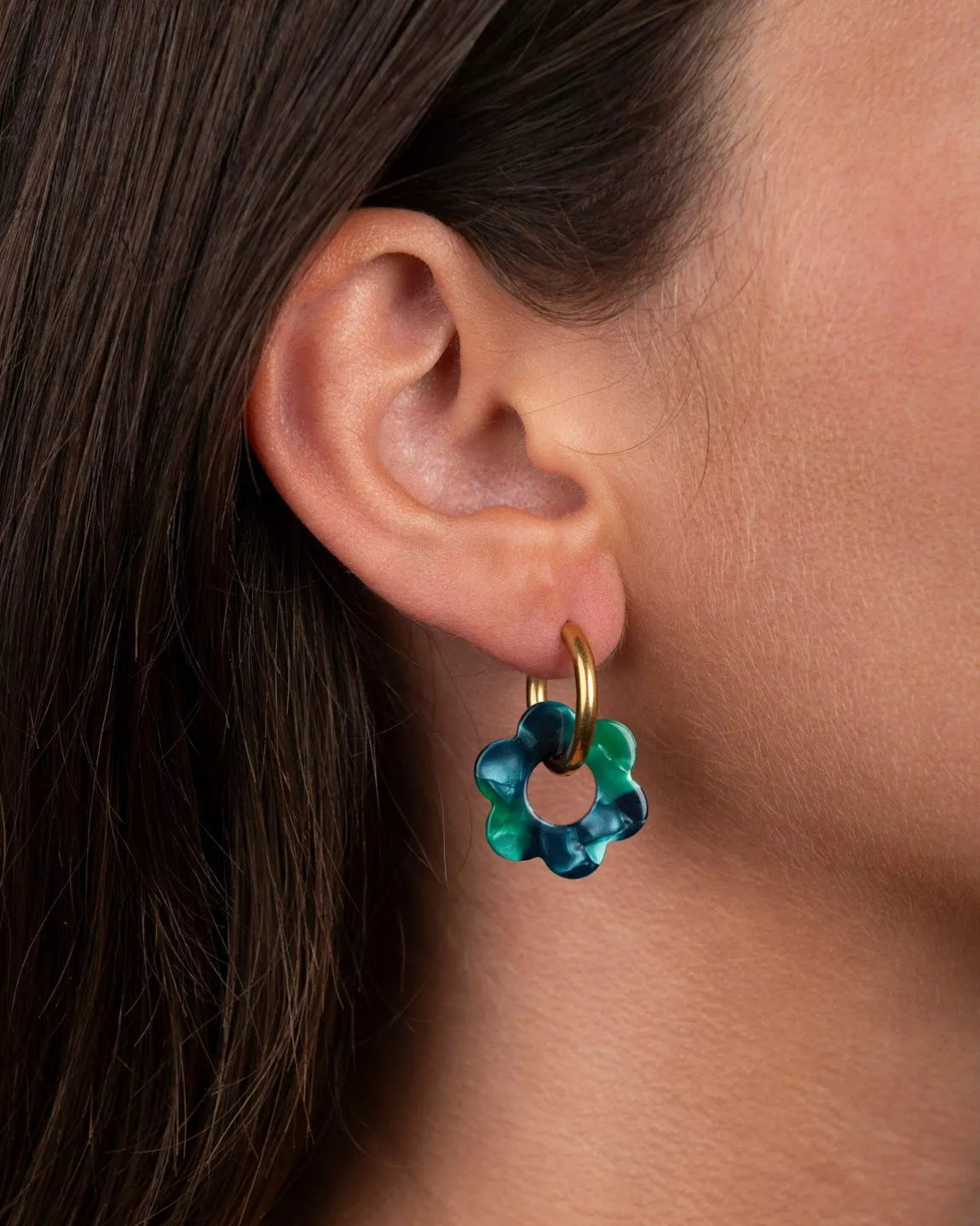 Boucles d’oreilles Baby Fleurette vert émeraude de Kurage portées à l’oreille, petites créoles dorées avec pendentifs en forme de fleur en acétate vert brillant.