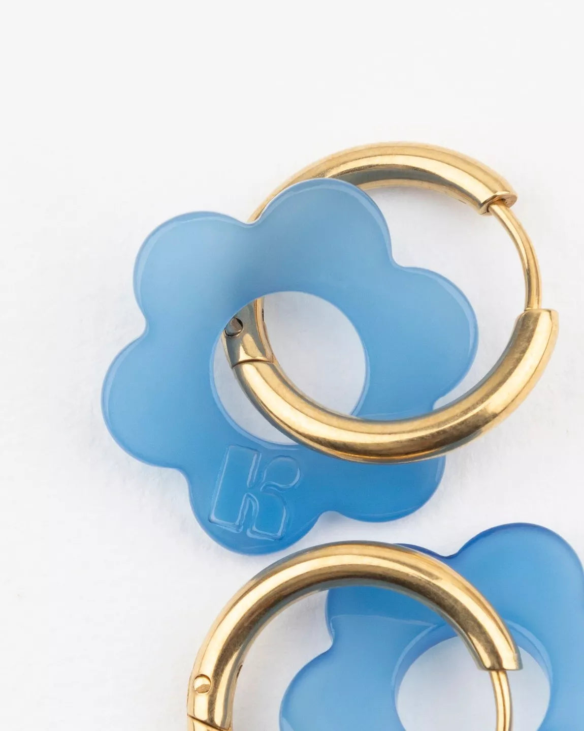 Détail des boucles d’oreilles BABY FLEURETTE Kurage Ginza – fleur en acétate bleu translucide gravée du logo K, sur anneau doré en acier inoxydable.
