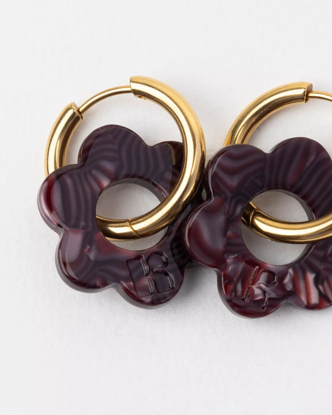Détail des boucles d’oreilles Baby Fleurette prune de Kurage, fleurs en acétate effet marbré prune foncé sur anneaux dorés.