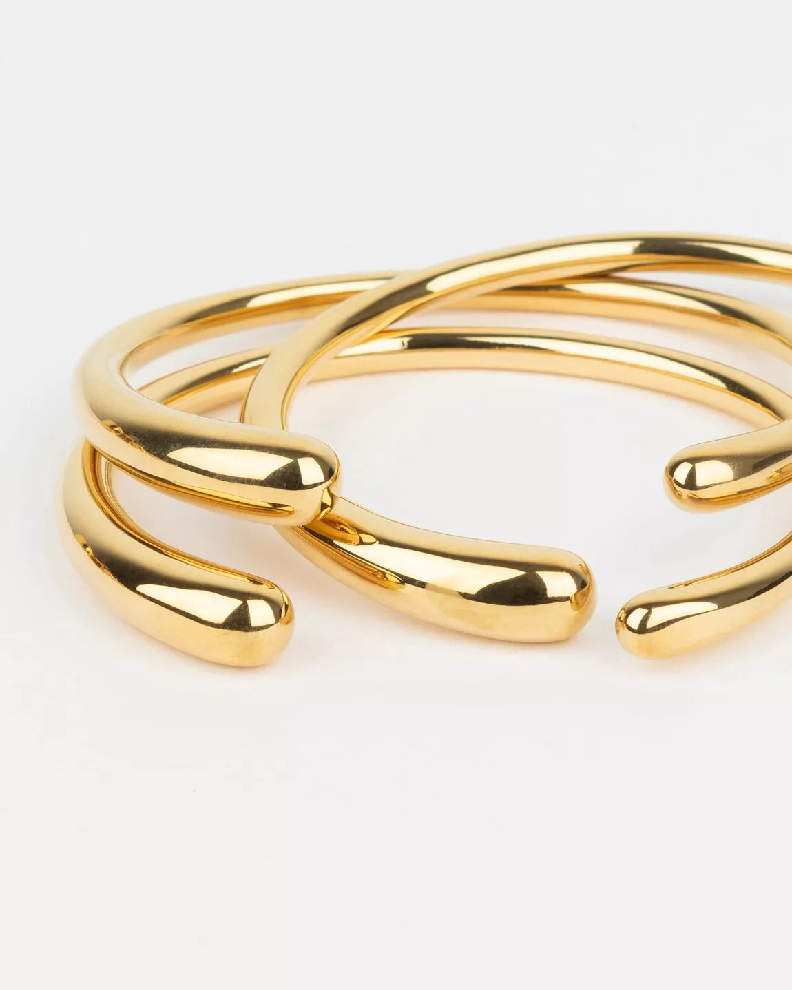 Détail du bracelet Galet de Kurage, joncs dorés en acier inoxydable aux extrémités arrondies, posés sur fond clair.