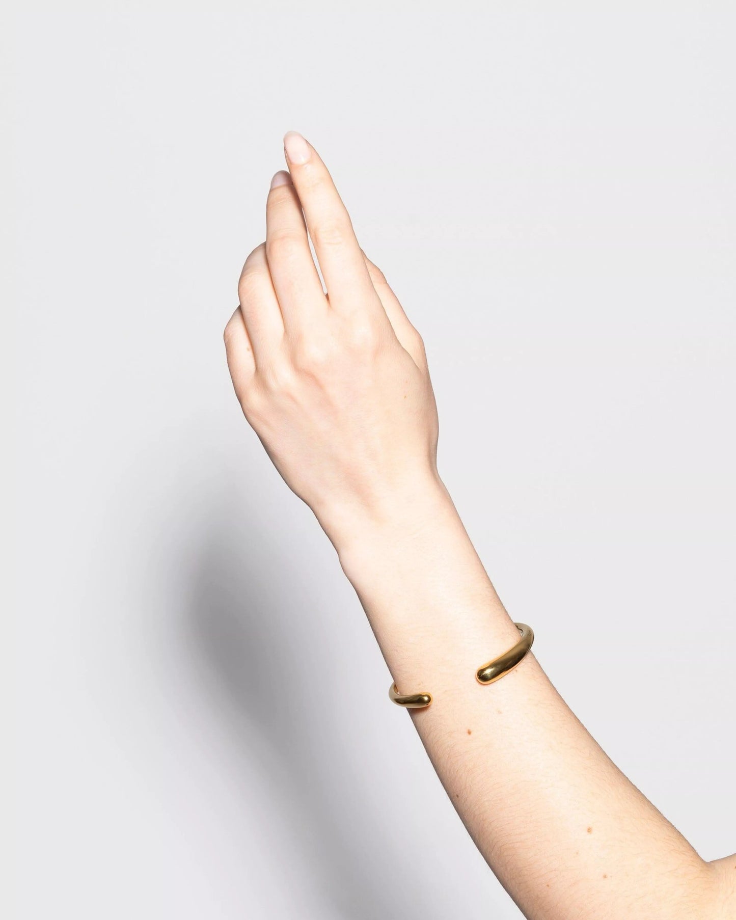 Bracelet Galet de Kurage porté au poignet, jonc doré ouvert aux extrémités arrondies sur fond blanc minimaliste.