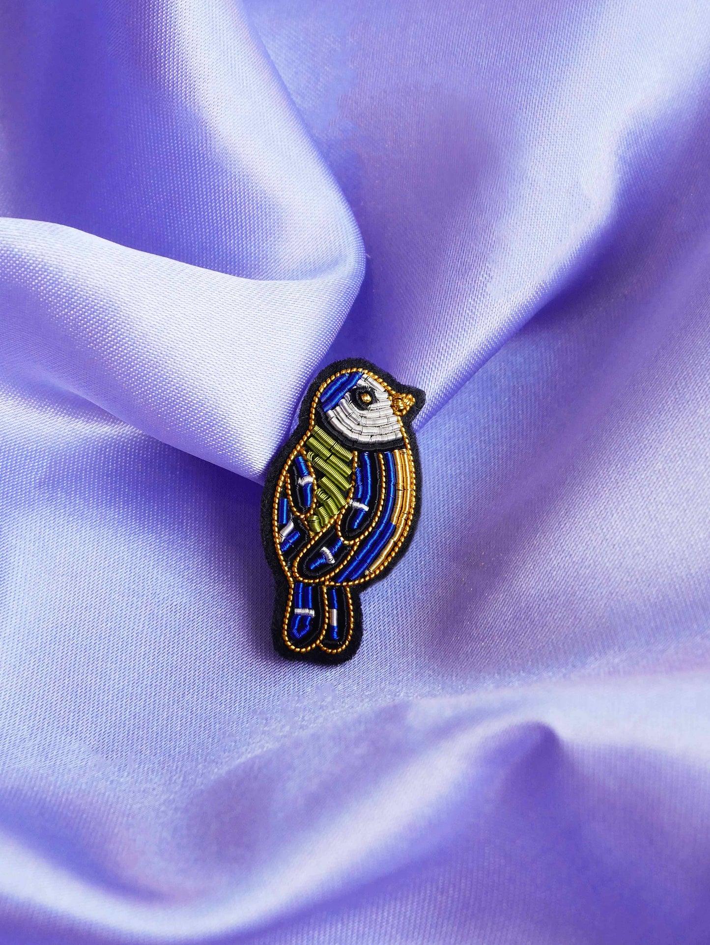 Gros plan de la broche Mésange posée sur tissu violet satiné.