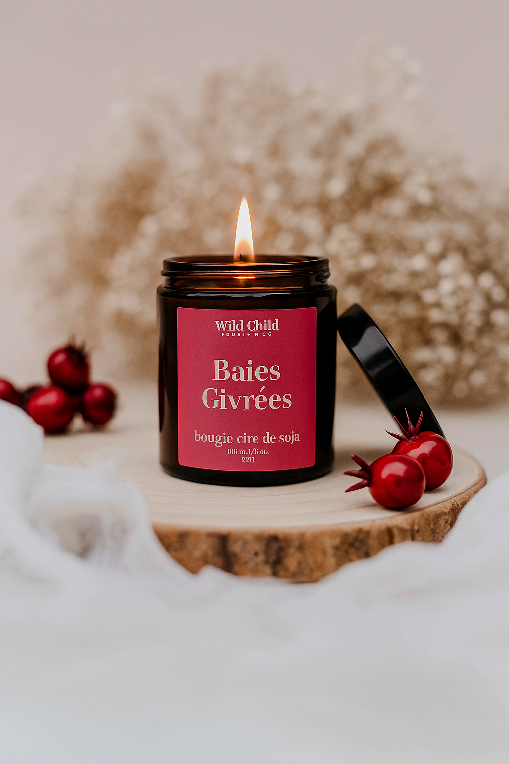 Bougie Baies Givrées allumée, en pot ambré, entourée de baies rouges et de décor hivernal, parfum fruité et épicé.