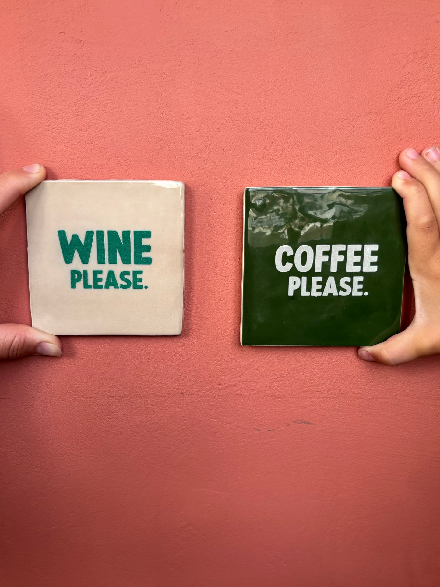 Carreaux en céramique artisanale Studio Meuk, tenus à la main devant un mur rose, avec inscriptions “WINE PLEASE” et “COFFEE PLEASE”. Décoration murale humoristique et artisanale vendue chez Anahata Concept Store.
