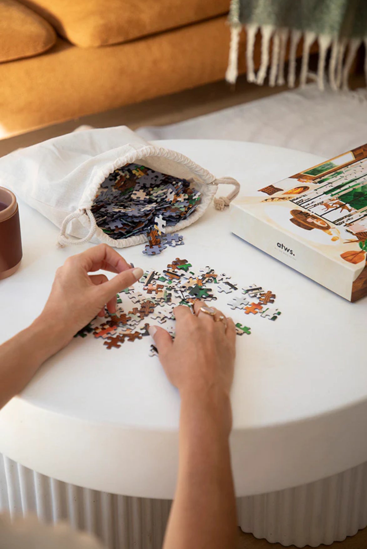 Zoom sur le puzzle Laponie 1000 pièces, mains en train d’assembler les morceaux avec la pochette en coton réutilisable et la boîte illustrée à côté.