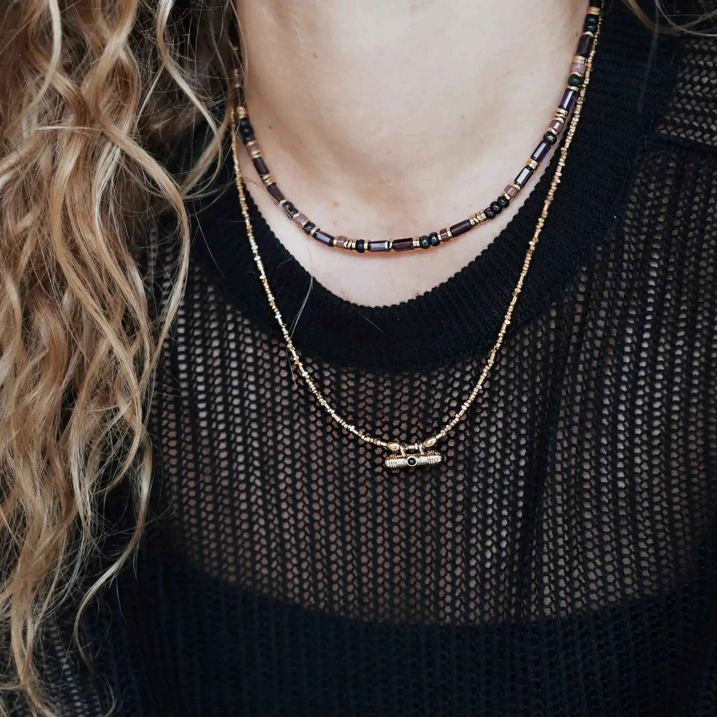 Gros plan du collier Roméa porté au ras du cou, composé de perles prune, noires et dorées, porté sur un haut noir en maille.