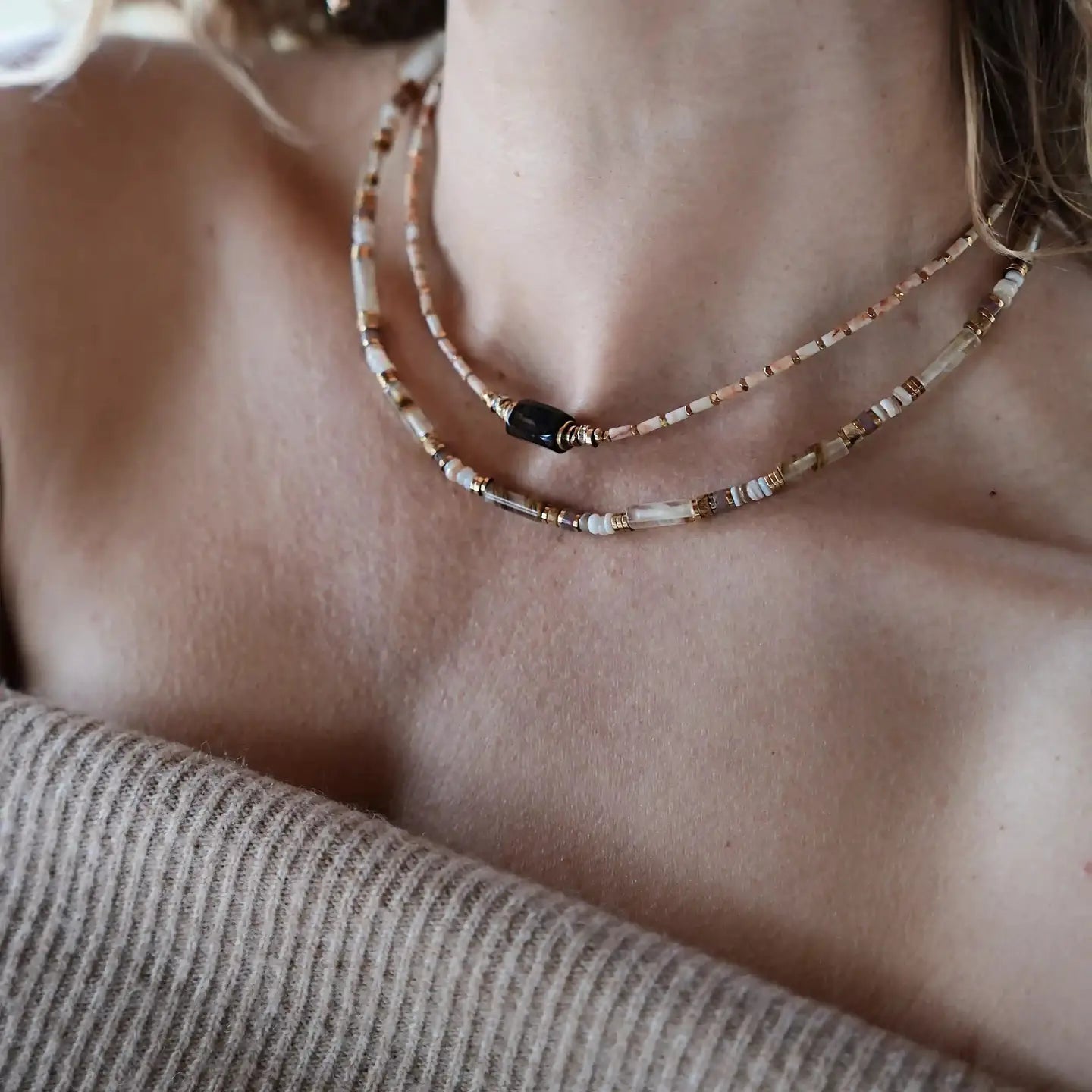 Collier Ysé Cloralys porté en superposition, perles beiges et pierre centrale noire, style bohème chic.