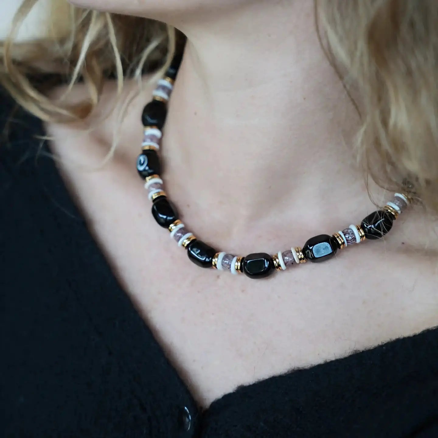 Gros plan du collier Hortense porté, composé de pierres noires et perles beige doré, Cloralys.