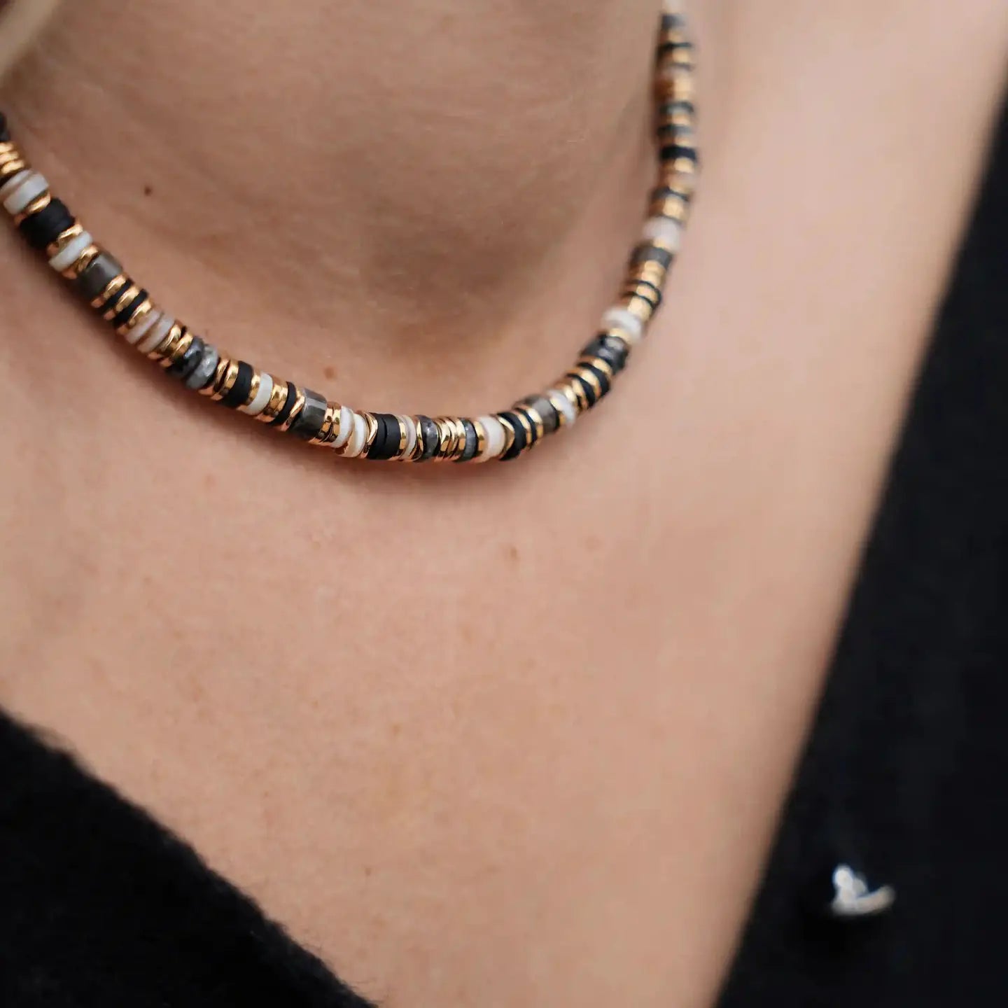 Gros plan sur le collier Elwood Noir Cloralys, perles heishi noires, dorées et naturelles, porté au ras du cou.