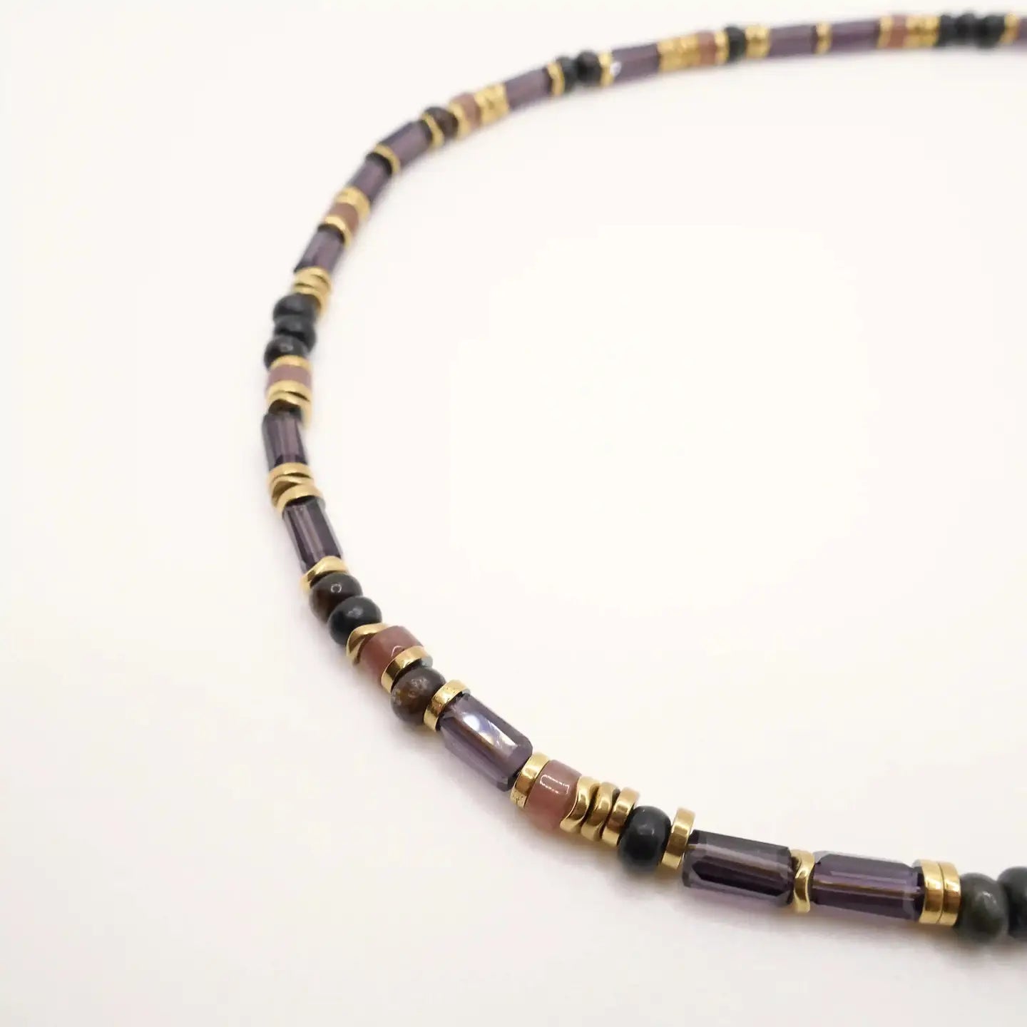 Détail du collier Roméa montrant les perles cylindriques prune et les perles rondes noires et dorées sur fond blanc.