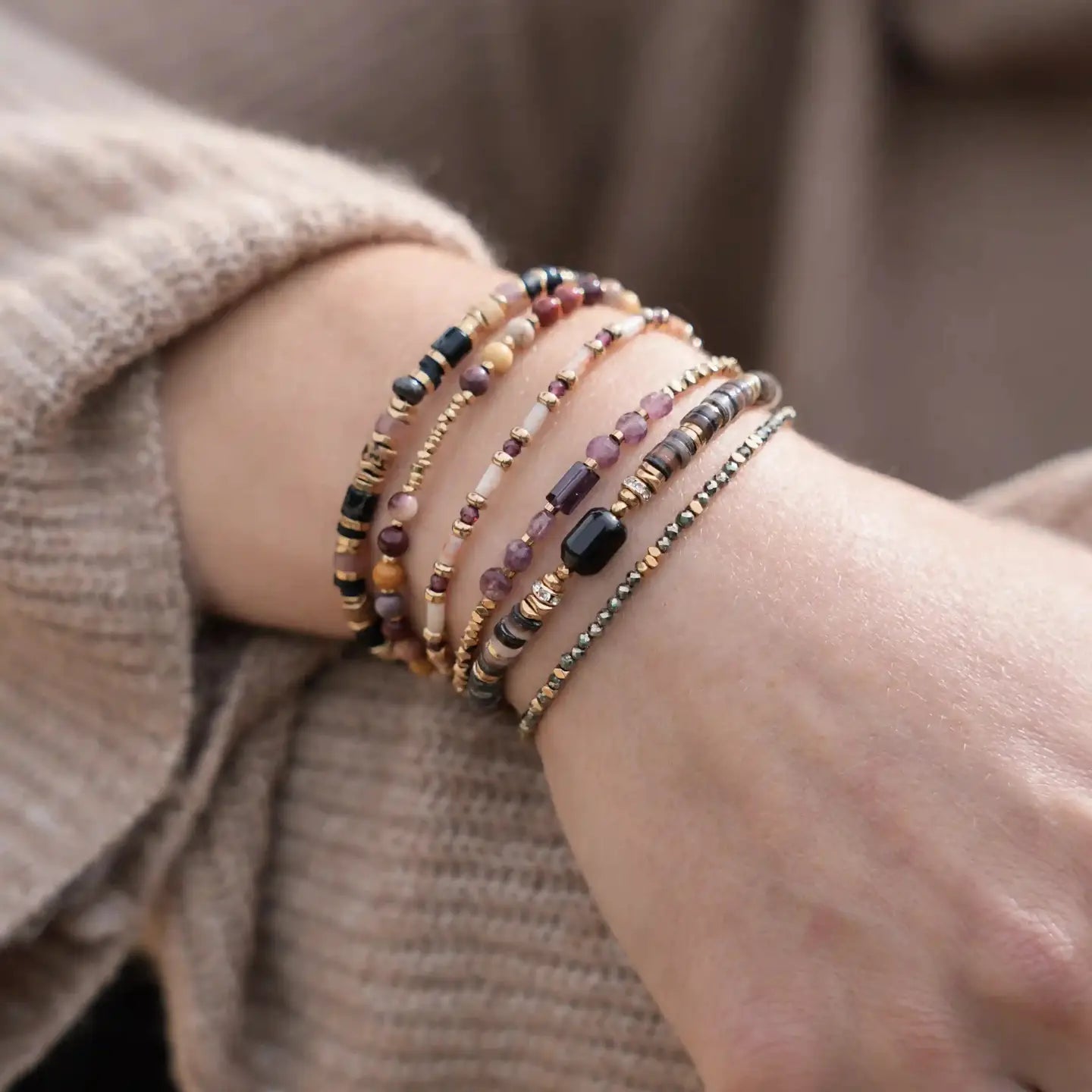 Poignet portant plusieurs bracelets fins, dont le bracelet Alix en Mokaïte, dans une accumulation de bijoux dorés et colorés