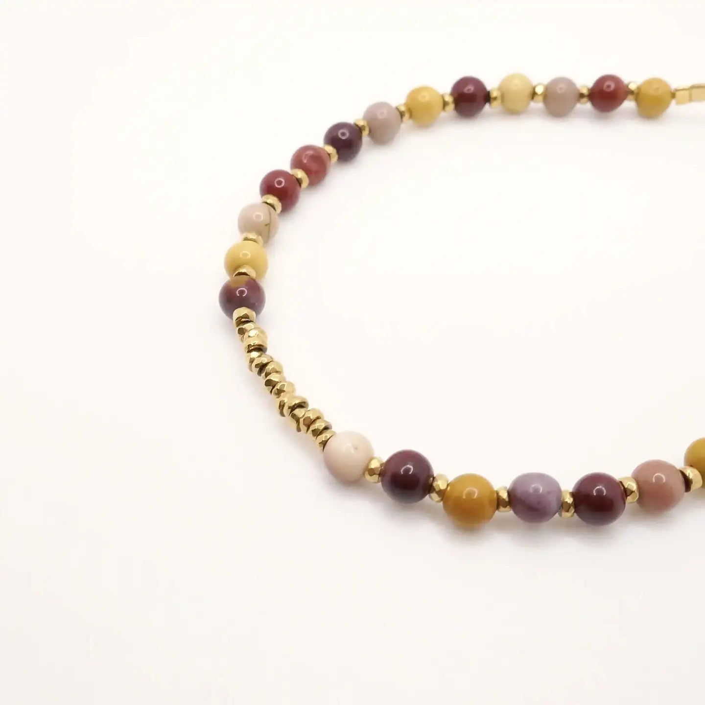 Gros plan sur le bracelet Alix composé de perles rondes en Mokaïte aux tons jaunes, prune et beige, avec des perles dorées en Hématite