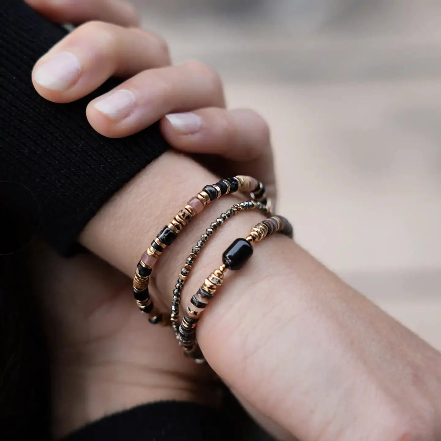 Bracelet Hermine porté au poignet, empilé avec d’autres bracelets dorés et noirs, créant un style élégant et moderne