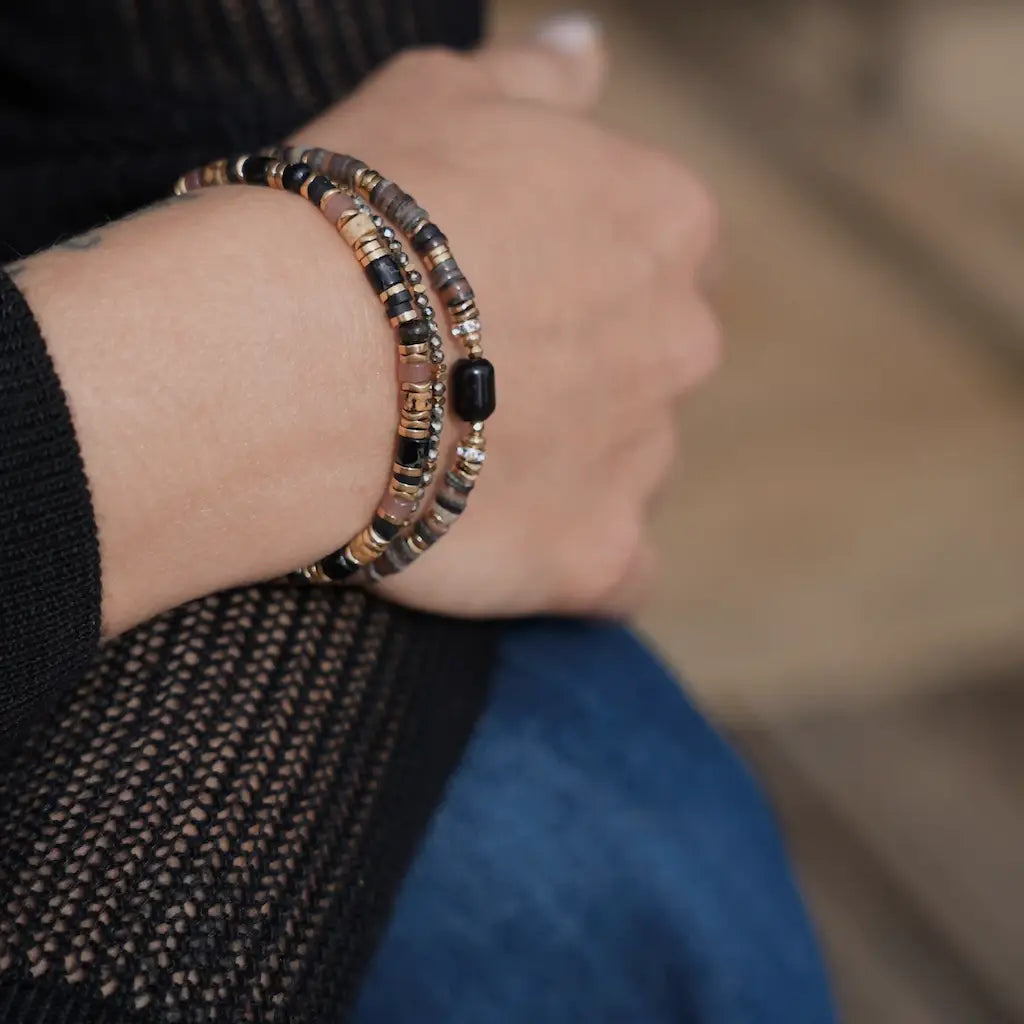  Bracelet Capucine porté au poignet, associé à d’autres bracelets fins dans des tons dorés, noirs et marron.