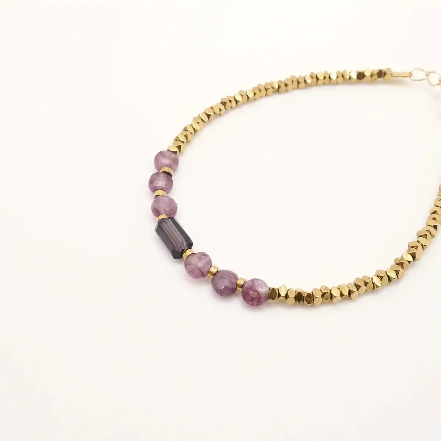 Gros plan sur le bracelet Zélie composé de perles dorées en hématite et de perles violettes en quartz d’Afrique, présenté sur fond blanc.