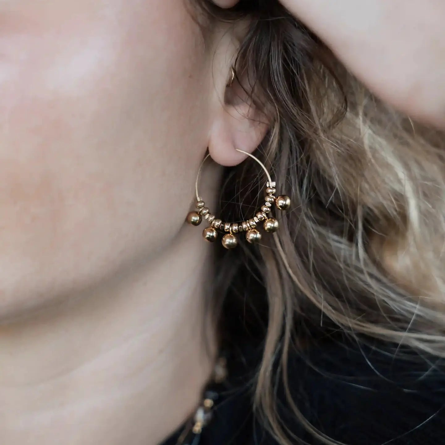 Gros plan sur une boucle d’oreille créole dorée Elvira portée, ornée de petites perles métalliques en hématite gold