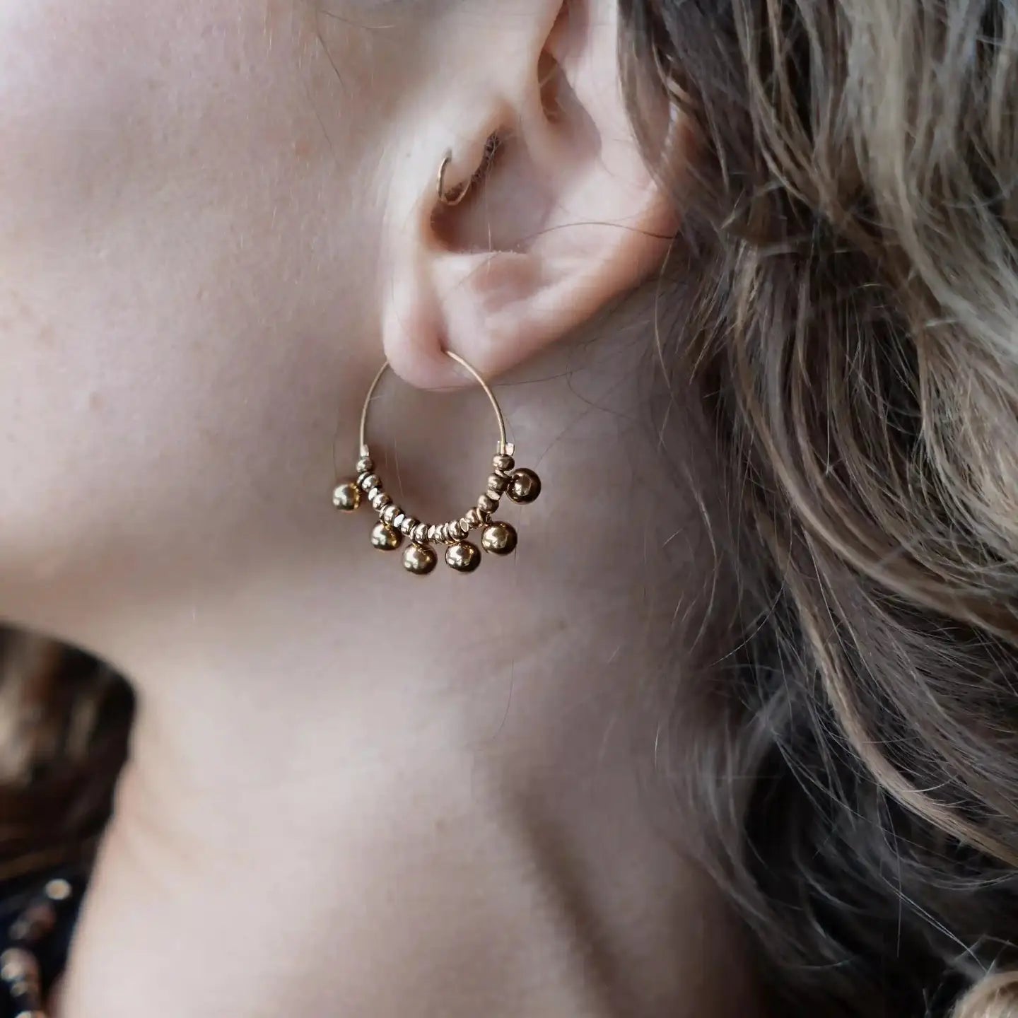 Boucle d’oreille créole Elvira portée, décorée de petites billes dorées en hématite gold
