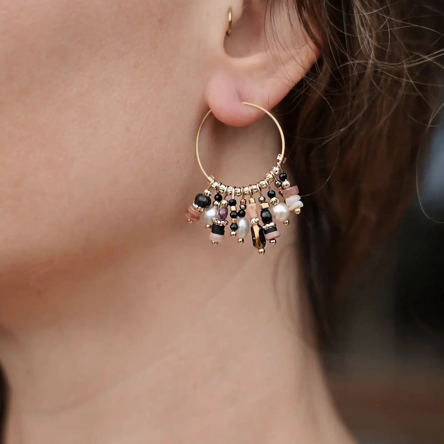 Boucle d’oreille créole Grace noire portée, ornée de perles naturelles noires, beige et nacrées.