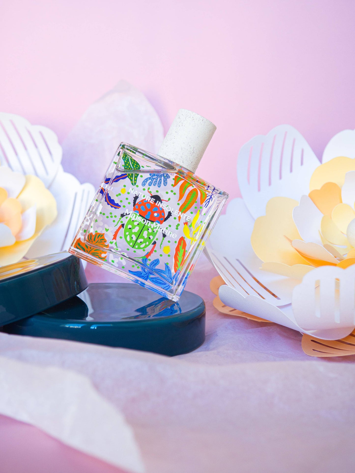 Flacon photographié sur fond rose et décor fleuri, ambiance poétique.