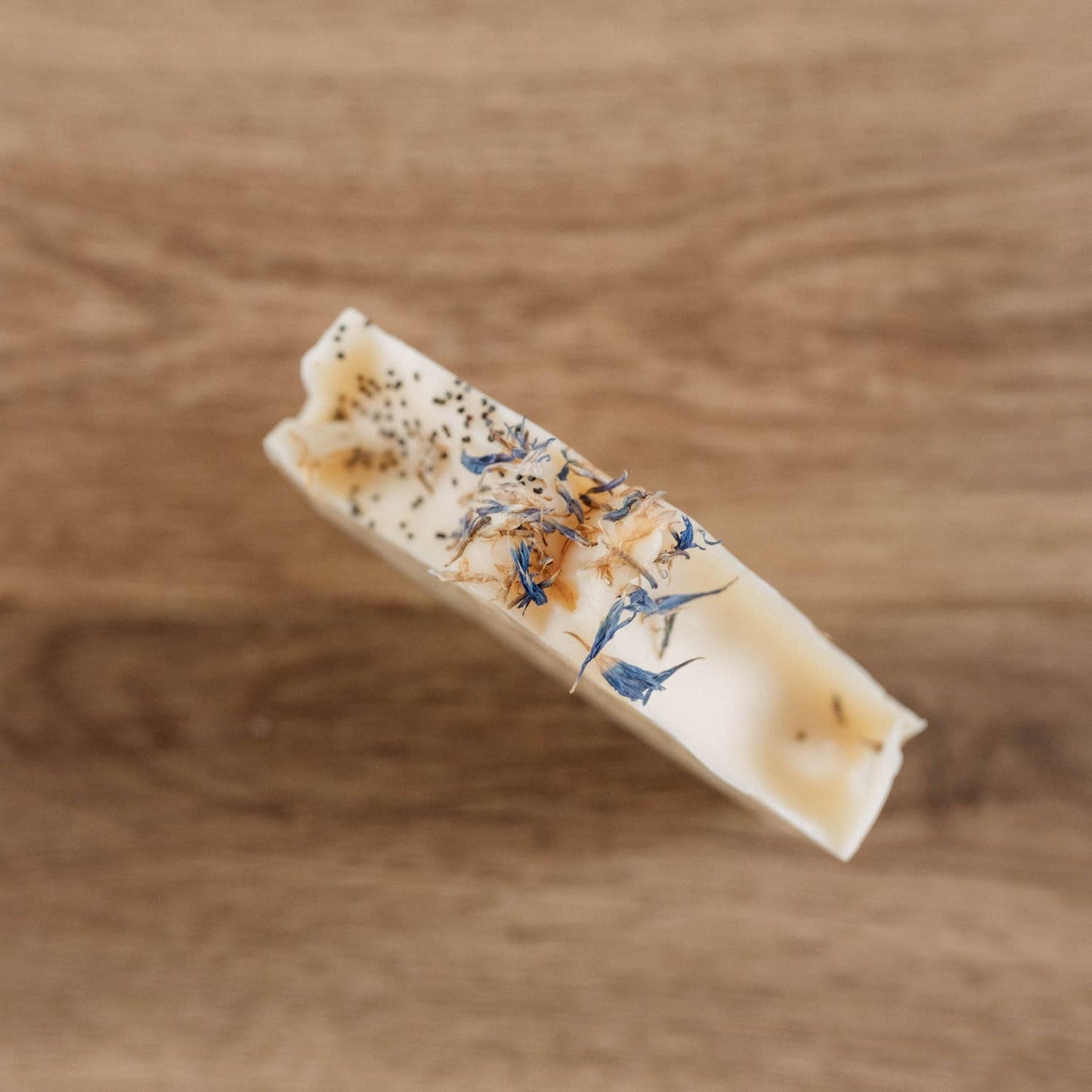 Tranche du savon Naturayl Karité Lait de Coco montrant sa texture crémeuse et ses pétales de fleurs séchées sur fond bois.