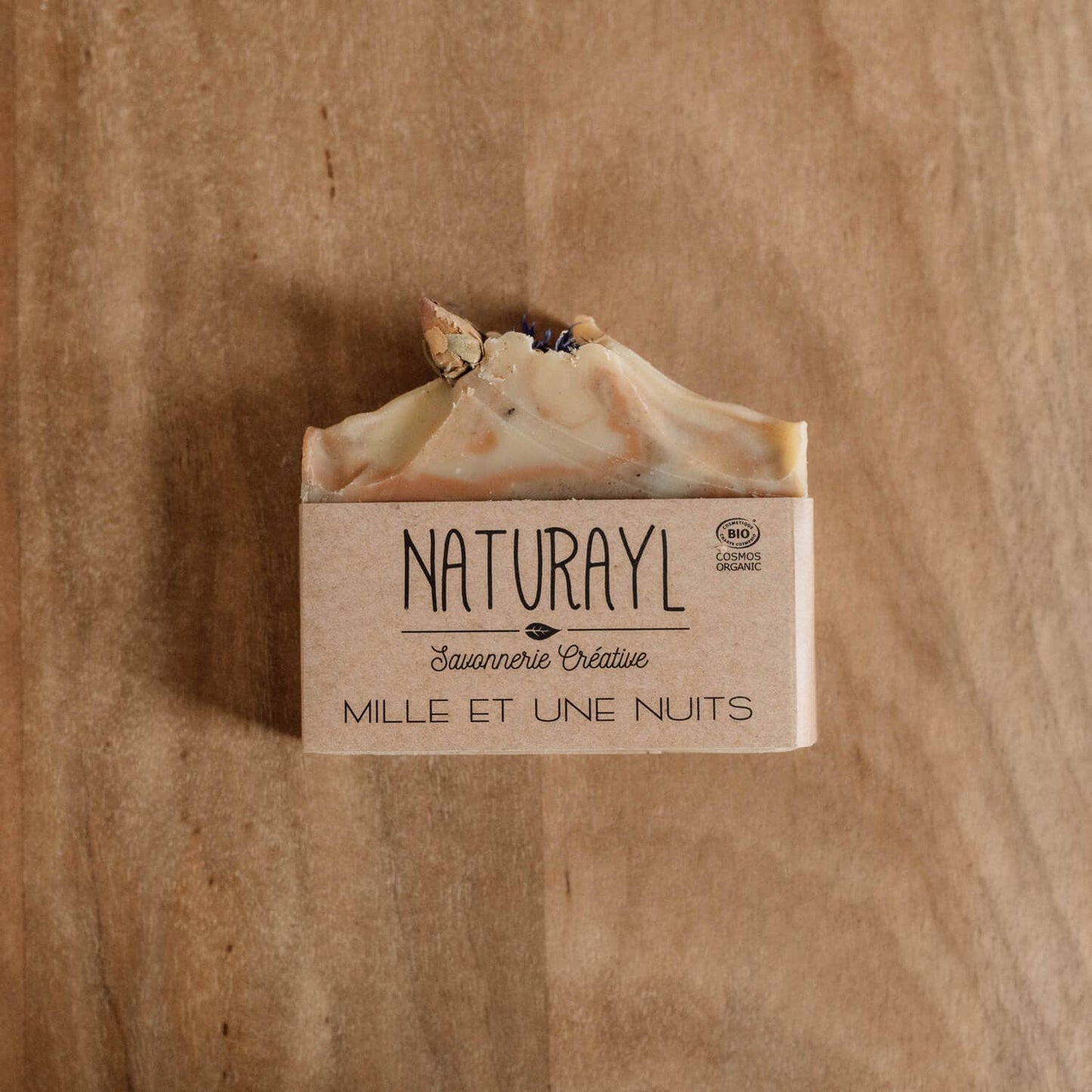 Savon Naturayl “Mille et une nuits” sur fond bois clair, mettant en avant l’étiquette et son aspect artisanal.