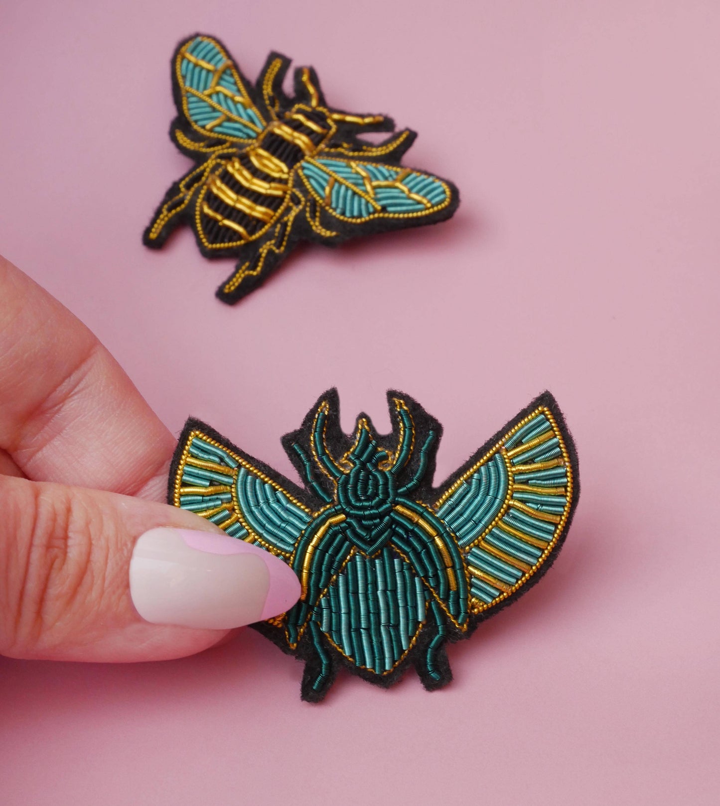 Broche abeille Malicieuse tenue en main, broderie dorée et verte.