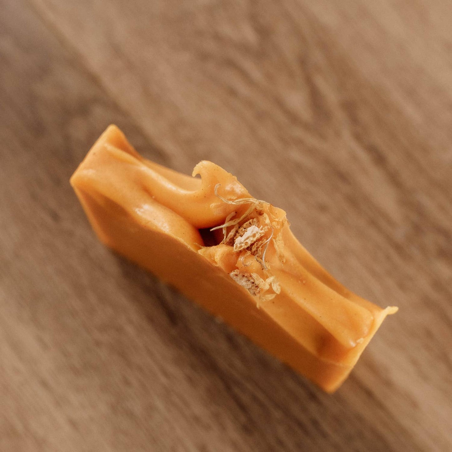 Tranche du savon Naturayl Orange Carotte montrant sa texture et ses inclusions végétales sur un fond en bois.