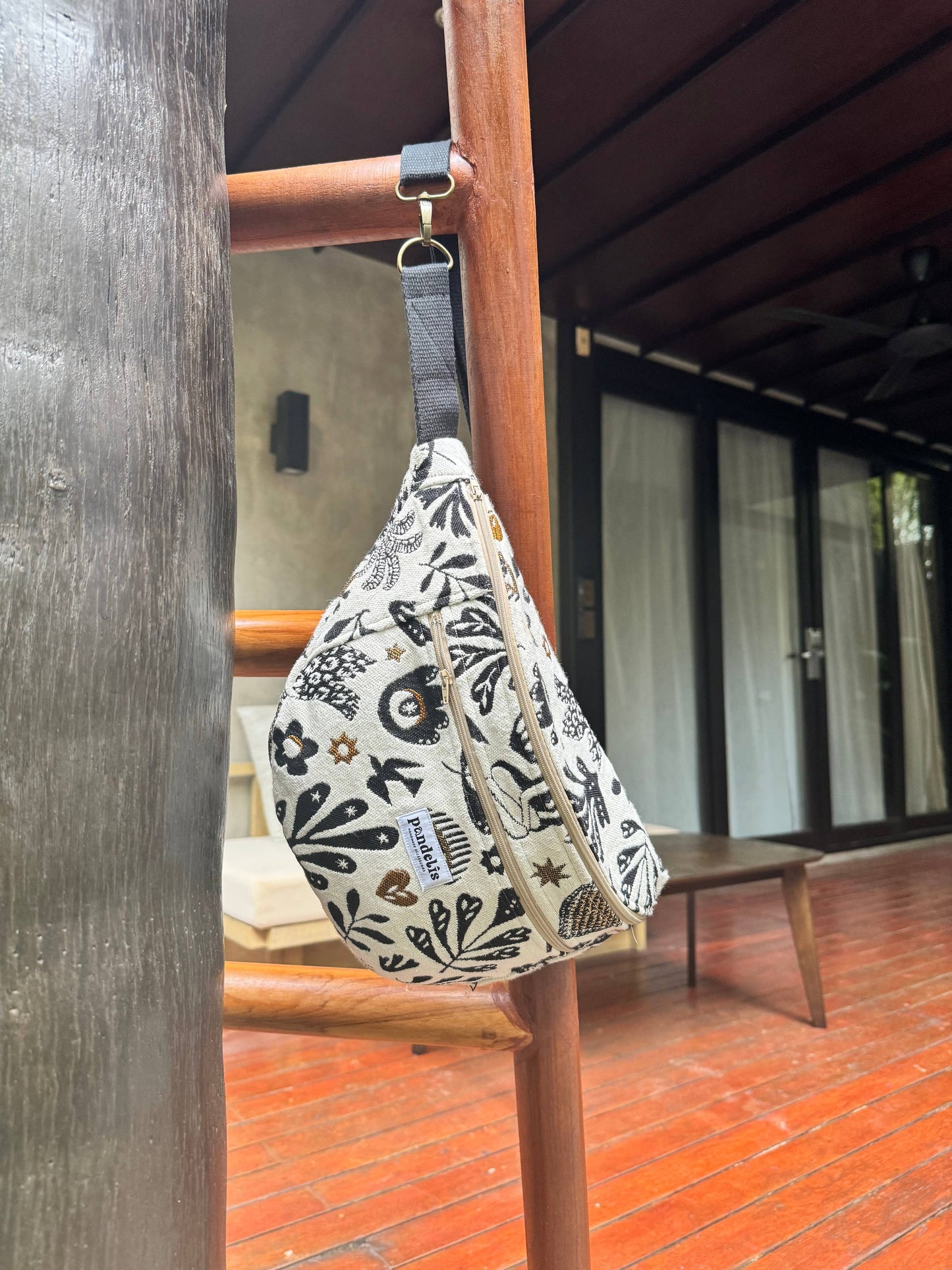  Grande banane Anthea Pandelis en velours écru à motifs noirs, suspendue à une rambarde en bois dans un décor naturel.