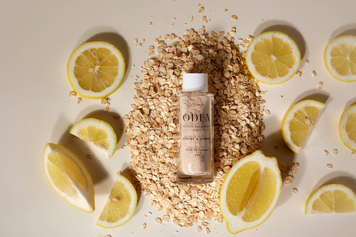  Flacon de poudre exfoliante posé sur un lit de tranches de citron frais et d’avoine