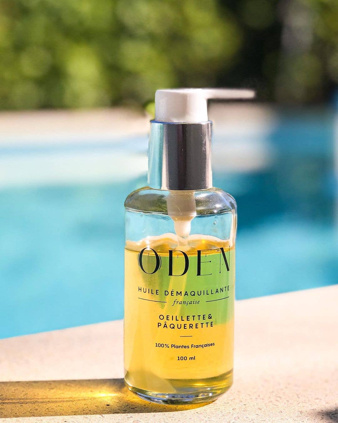 Flacon d’huile démaquillante posé au bord d’une piscine, ambiance estivale