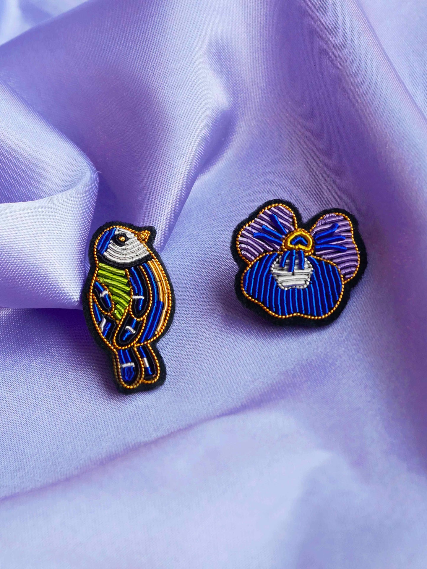 Gros plan de la broche Mésange avec une autre broche posées sur tissu violet satiné.