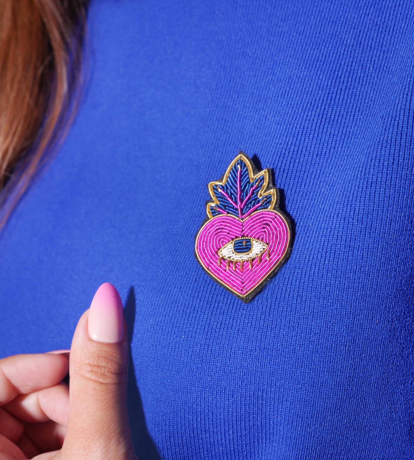 Broche Ex Voto Pink portée sur un vêtement bleu, mise en valeur par un contraste coloré et un détail raffiné de la broderie.