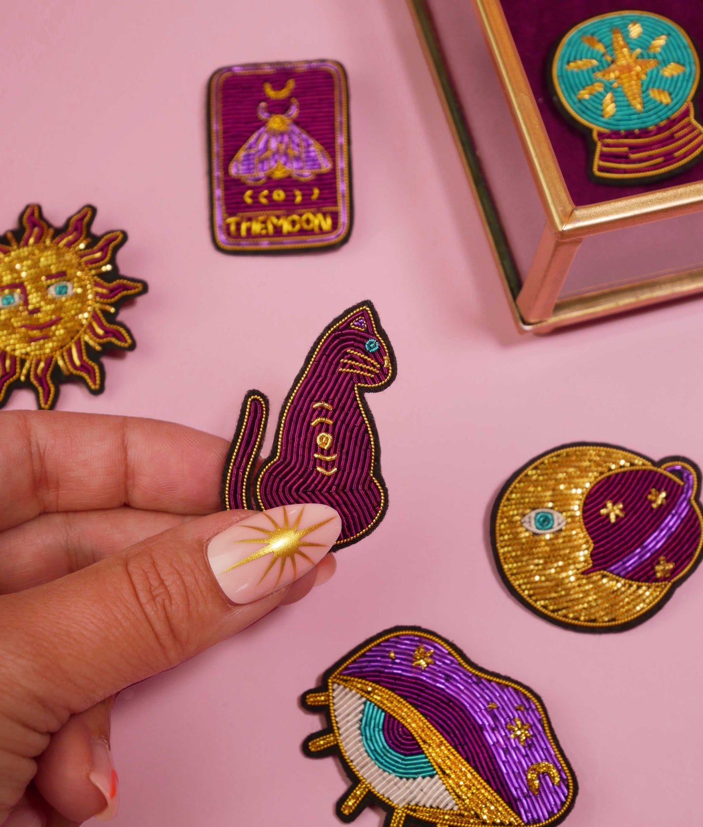 Broche Cat Magic Malicieuse tenue en main, entourée d’autres broches brodées colorées