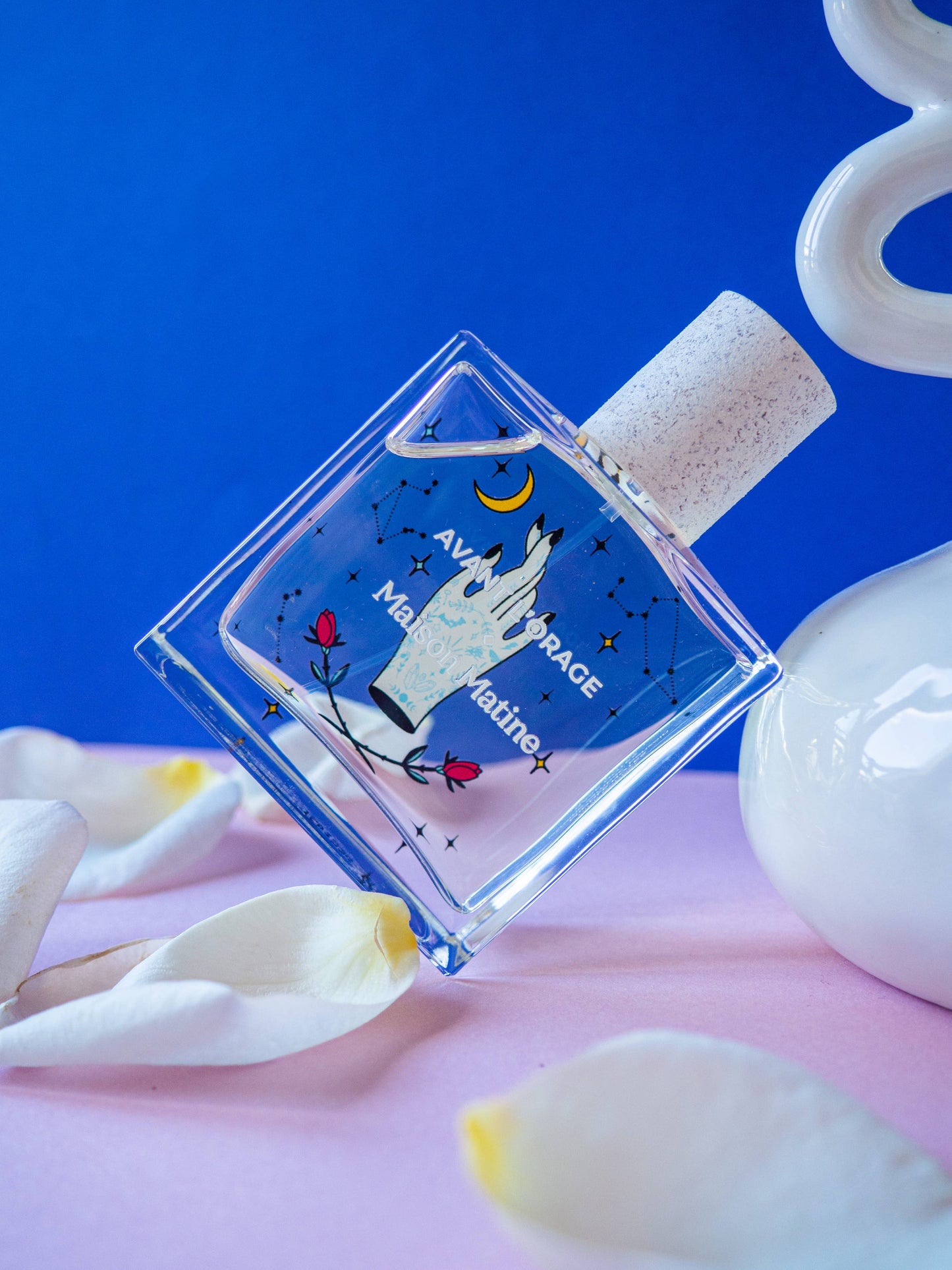 Flacon du parfum Avant l’Orage posé sur fond bleu avec pétales blancs.