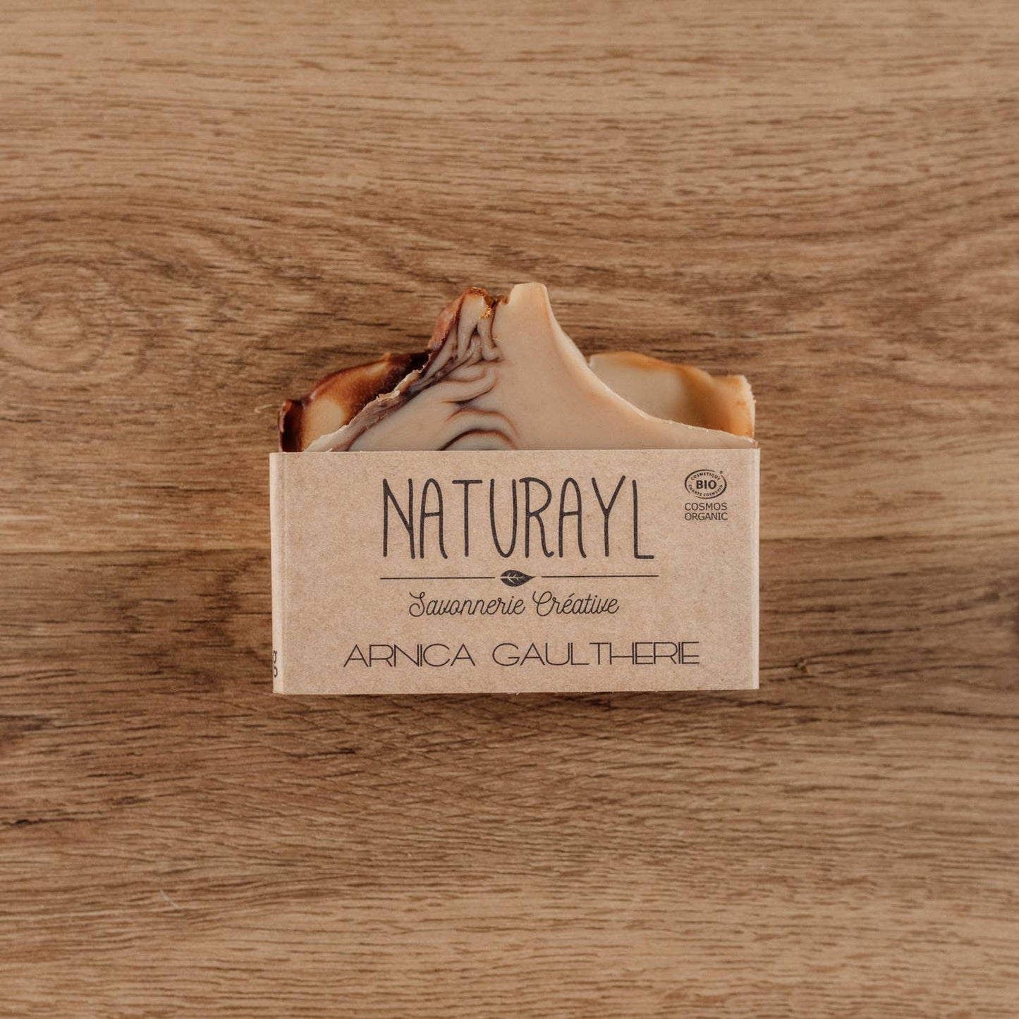 Savon solide Naturayl Arnica Gaulthérie posé sur une surface en bois, avec son emballage kraft artisanal.